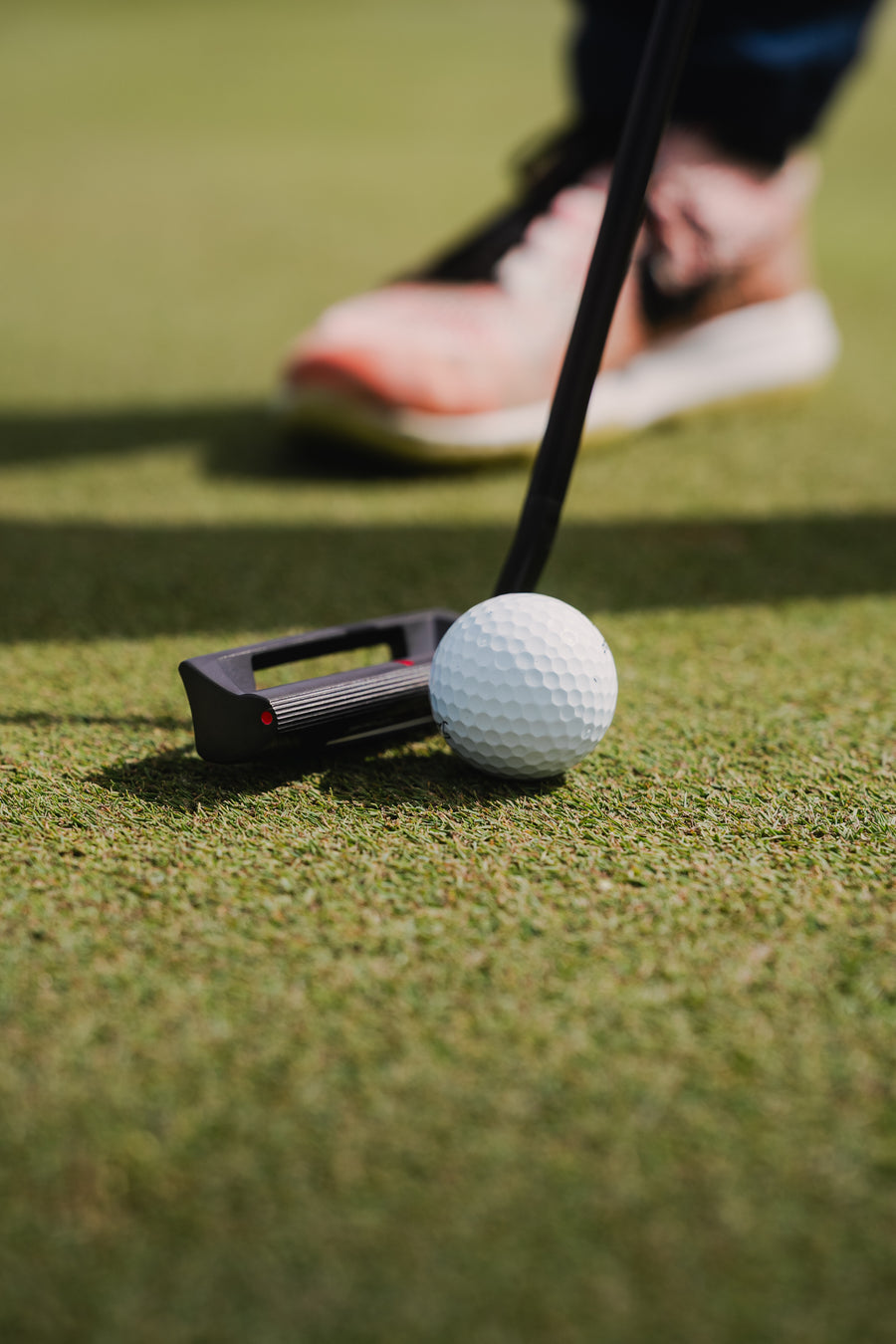 A blade putter resting on the turf beside a ball